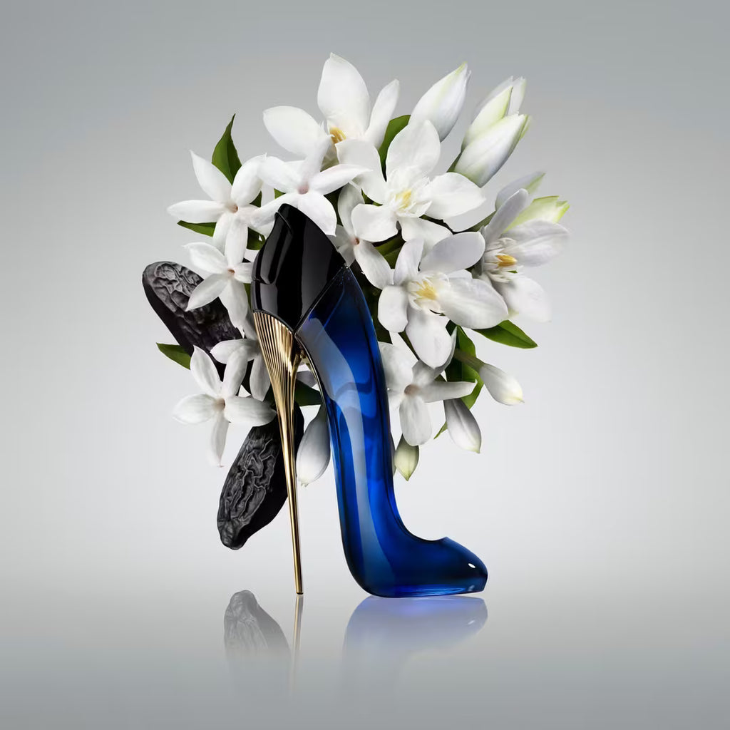 Blue high-heeled shoe with gold heel on a bed of white flowers against a gray background