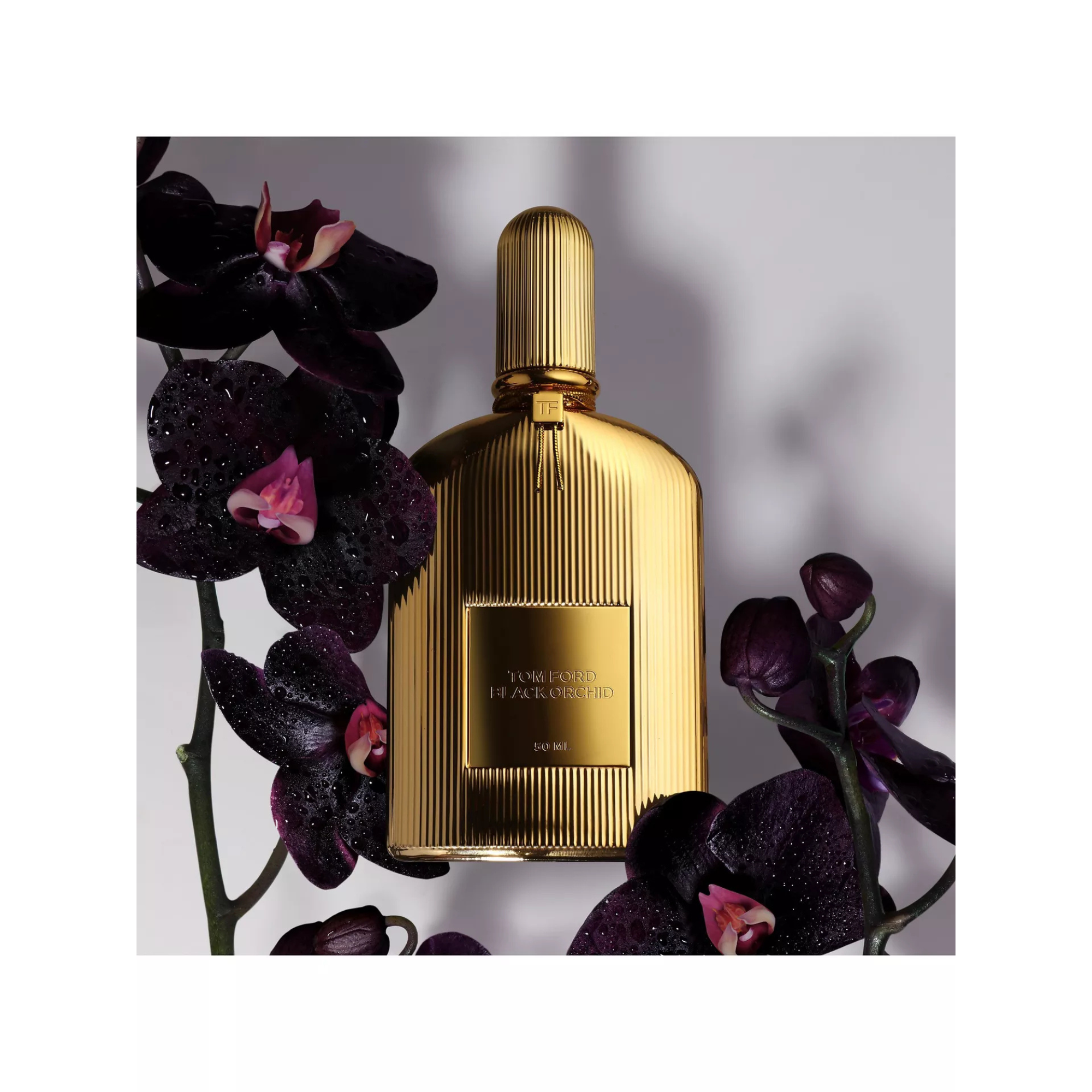 Gold perfume bottle with dark purple orchids on a light gray background