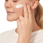 Woman applying cream to her face with a white background